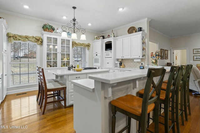 kitchen featuring pendant lighting, a breakfast bar area, a center island, white cabinets, and light wood-type flooring