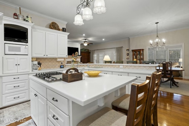 kitchen with white microwave, a kitchen breakfast bar, kitchen peninsula, and white cabinets