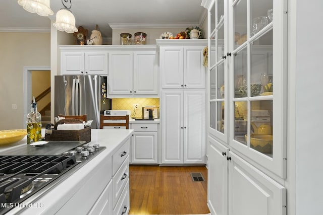 kitchen with white cabinetry, backsplash, hanging light fixtures, stainless steel appliances, and crown molding