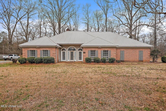 view of front facade featuring metal roof, a chimney, a front lawn, and brick siding