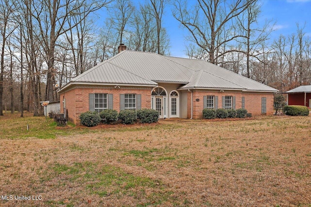 view of front of house with metal roof, a chimney, a front lawn, and brick siding