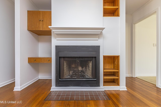 interior details featuring a fireplace with flush hearth, crown molding, baseboards, and wood finished floors