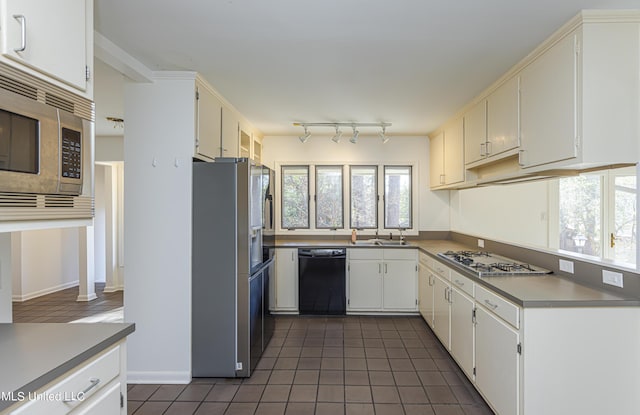 kitchen with appliances with stainless steel finishes, a sink, dark tile patterned floors, white cabinetry, and track lighting