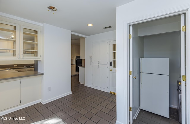 kitchen with visible vents, baseboards, glass insert cabinets, freestanding refrigerator, and dark tile patterned floors