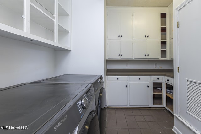 laundry area with dark tile patterned floors, washer and clothes dryer, and cabinet space