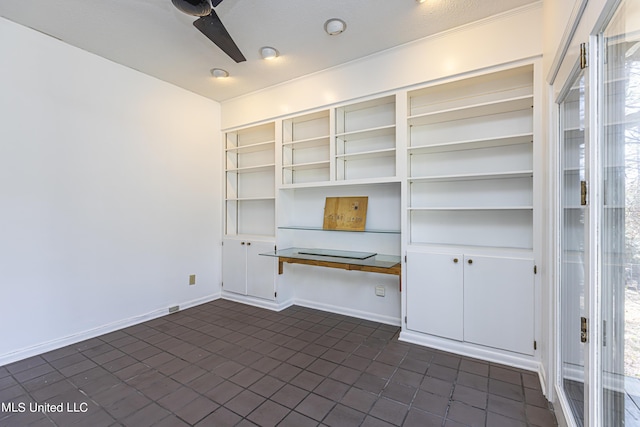 unfurnished office with a ceiling fan, built in desk, and baseboards