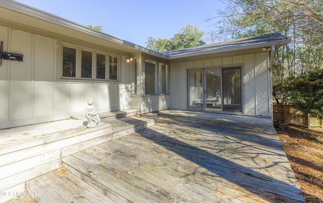 doorway to property with board and batten siding, fence, and a wooden deck