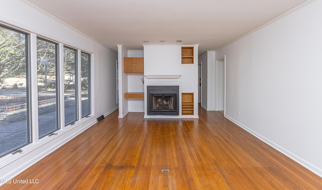 unfurnished living room with hardwood / wood-style flooring, baseboards, a fireplace with raised hearth, and crown molding