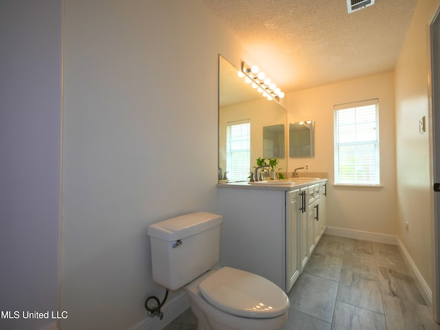 bathroom with vanity, visible vents, baseboards, a textured ceiling, and toilet