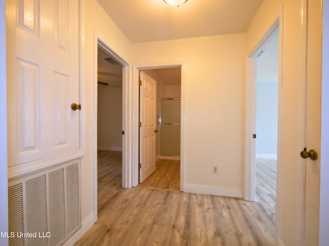 hallway featuring light wood-type flooring, visible vents, baseboards, and a textured ceiling