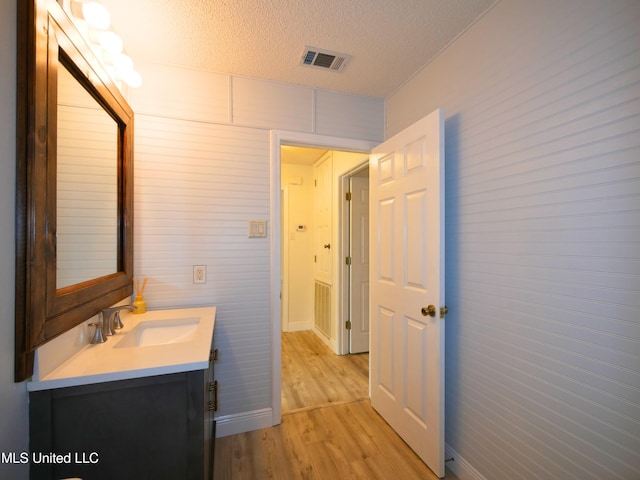 bathroom featuring vanity, wood finished floors, baseboards, visible vents, and a textured ceiling