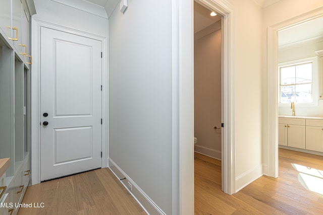 corridor with ornamental molding, sink, and light hardwood / wood-style flooring