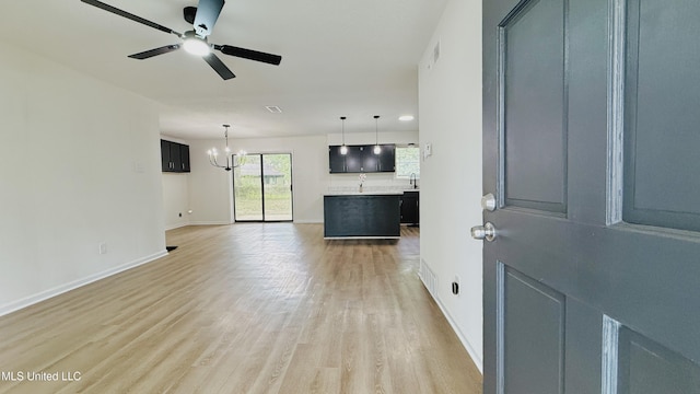 unfurnished living room featuring a chandelier, light wood-style flooring, ceiling fan, baseboards, and a sink
