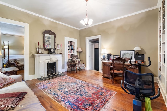 home office with a fireplace with raised hearth, hardwood / wood-style flooring, baseboards, ornamental molding, and an inviting chandelier