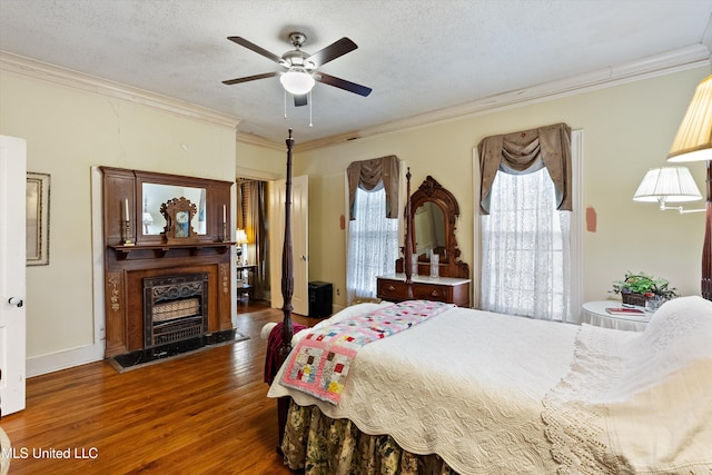 bedroom with a fireplace with raised hearth, crown molding, a textured ceiling, and wood finished floors