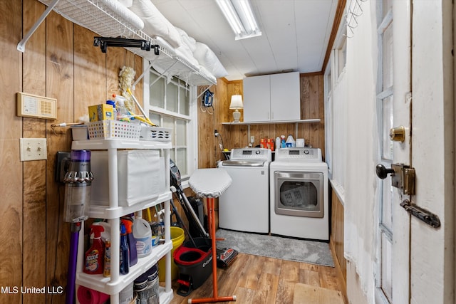 laundry area featuring wood walls, independent washer and dryer, cabinet space, and light wood-style floors