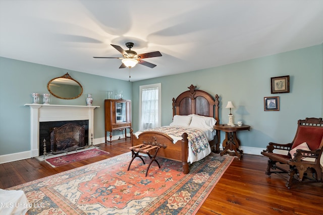 bedroom with a fireplace with flush hearth, baseboards, hardwood / wood-style floors, and a ceiling fan