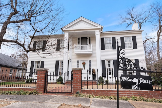 neoclassical / greek revival house featuring a balcony and a fenced front yard