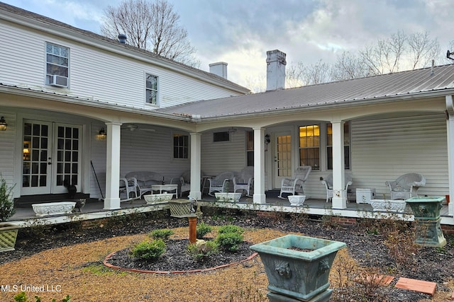 rear view of property featuring covered porch, a chimney, metal roof, and french doors