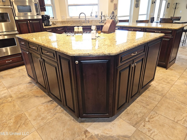 kitchen with a kitchen island, stainless steel appliances, sink, dark brown cabinetry, and light stone counters