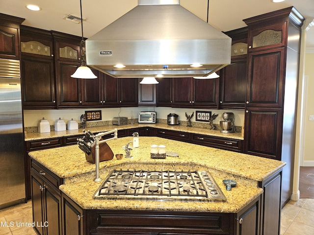 kitchen featuring hanging light fixtures, stainless steel appliances, range hood, a center island with sink, and light stone counters