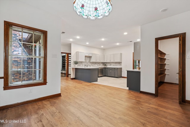 kitchen featuring gray cabinetry, light hardwood / wood-style flooring, stainless steel dishwasher, backsplash, and a chandelier