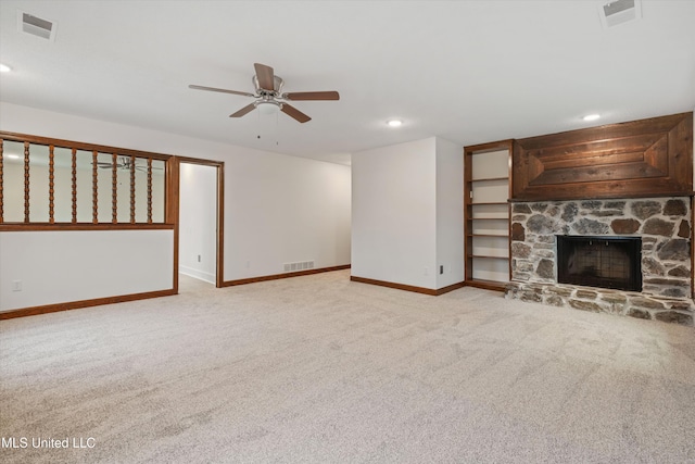 unfurnished living room with ceiling fan, a stone fireplace, and light colored carpet