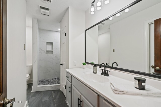 bathroom featuring tiled shower, tile patterned floors, vanity, and toilet