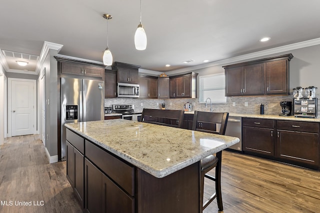 kitchen with dark brown cabinetry, dark wood-style flooring, appliances with stainless steel finishes, a center island, and decorative light fixtures