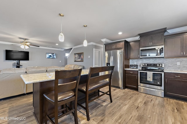 kitchen with appliances with stainless steel finishes, open floor plan, dark brown cabinets, and pendant lighting