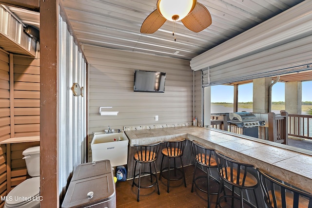 interior space featuring a dry bar, wood walls, ceiling fan, and dark wood-type flooring