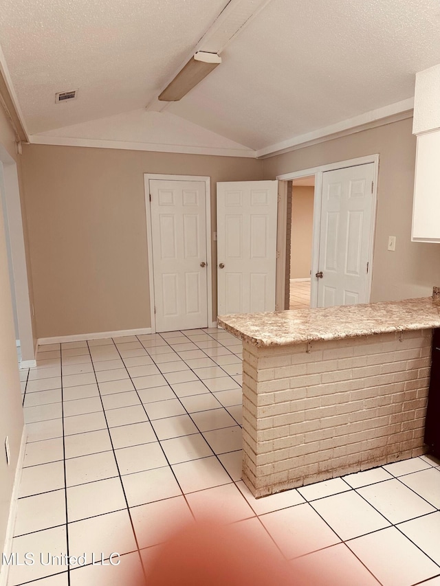 143 James Dr, Gulfport, MS 39503 - kitchen with lofted ceiling, a peninsula, light tile patterned floors, baseboards, and a textured ceiling