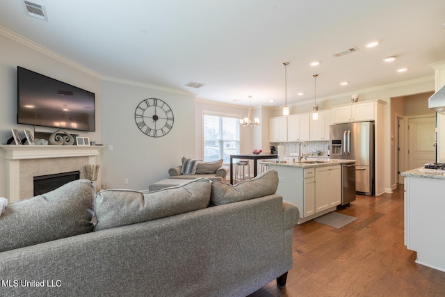 living room featuring sink, a fireplace, hardwood / wood-style floors, crown molding, and a chandelier