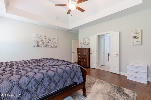 bedroom with a raised ceiling, wood-type flooring, and ceiling fan