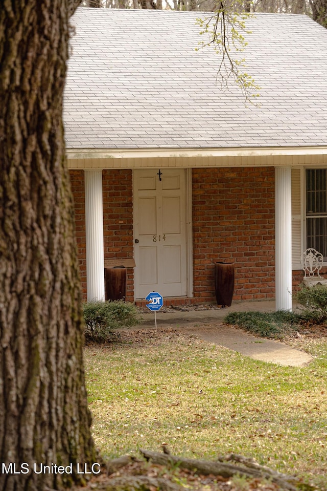 doorway to property featuring a lawn and brick siding