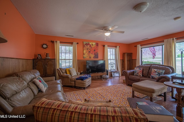living area featuring a textured ceiling, a wainscoted wall, visible vents, ceiling fan, and wood finished floors