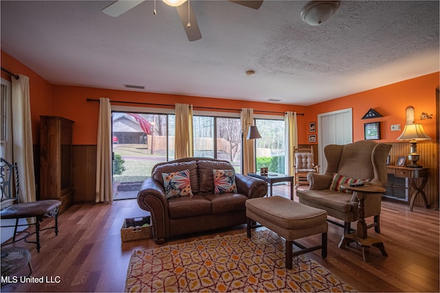 living room featuring a textured ceiling, visible vents, ceiling fan, wood finished floors, and wainscoting