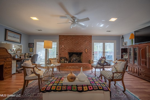 living area with a fireplace, a ceiling fan, light wood-style floors, and crown molding