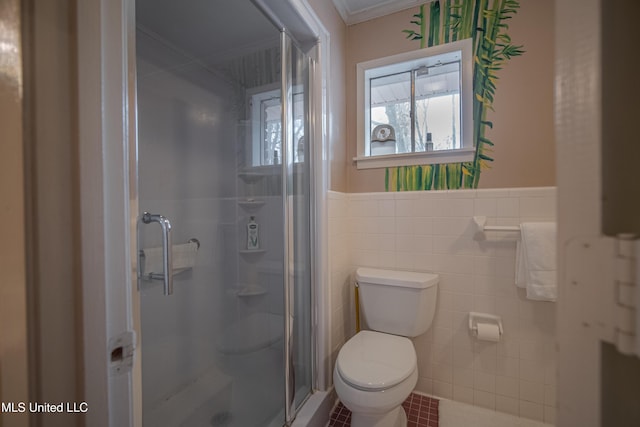 bathroom with tile walls, toilet, ornamental molding, a shower stall, and a wainscoted wall