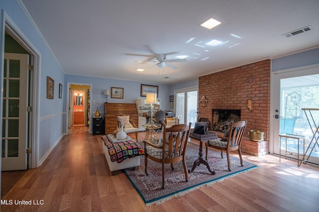 living room with wood finished floors, crown molding, a fireplace, and visible vents