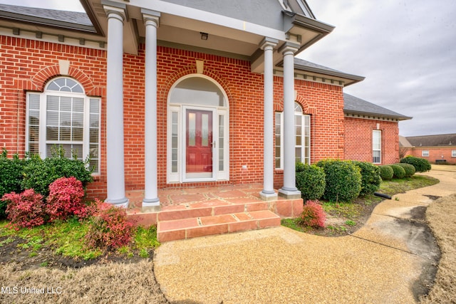 view of exterior entry with roof with shingles and brick siding