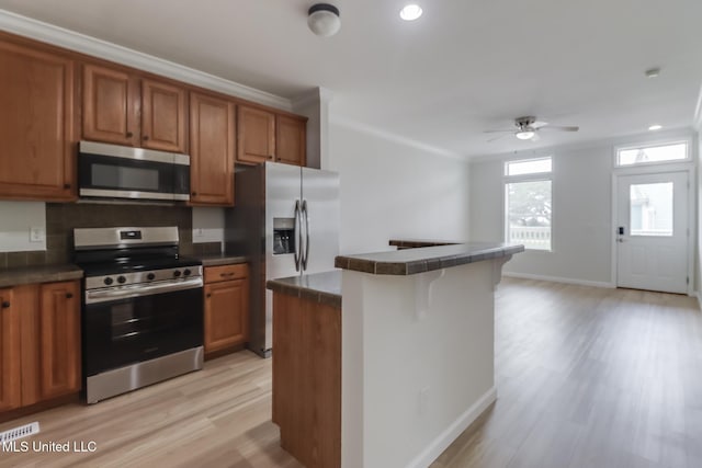 1515 E Beach Blvd Unit 132, Pass Christian, MS 39571 - kitchen featuring appliances with stainless steel finishes, a ceiling fan, light wood-style floors, brown cabinetry, and crown molding