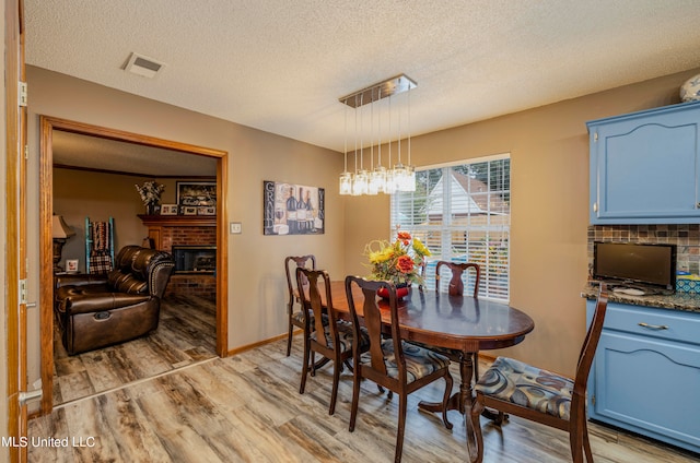 dining space featuring light hardwood / wood-style flooring, a textured ceiling, and a brick fireplace