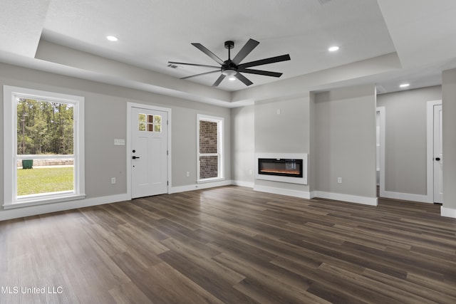 1457 Rue De Courmont, Gautier, MS 39553 - unfurnished living room with dark wood-style flooring, ceiling fan, a raised ceiling, a glass covered fireplace, and recessed lighting