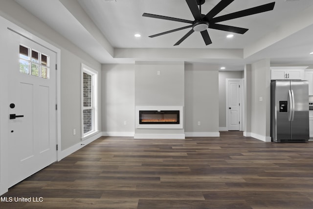 1457 Rue De Courmont, Gautier, MS 39553 - unfurnished living room featuring a glass covered fireplace, a ceiling fan, dark wood-style floors, recessed lighting, and a tray ceiling