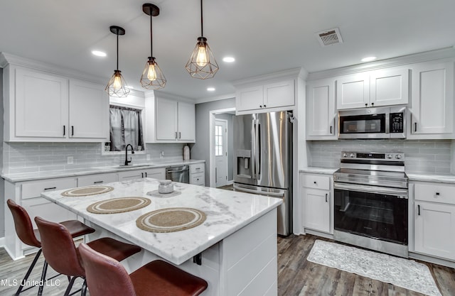 kitchen featuring decorative light fixtures, stainless steel appliances, a center island, and white cabinets