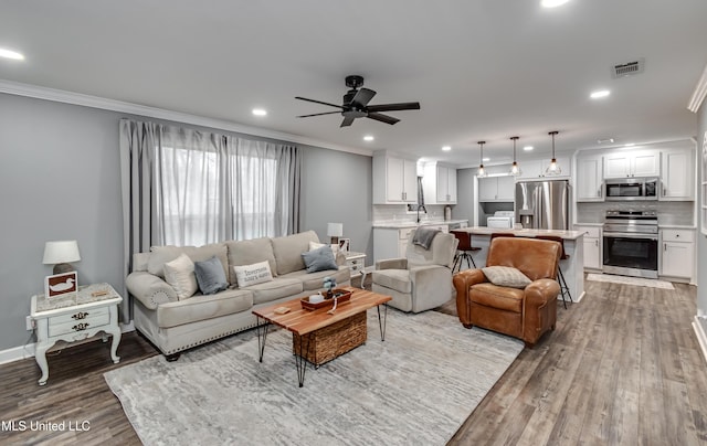 living room with crown molding, ceiling fan, sink, and light wood-type flooring