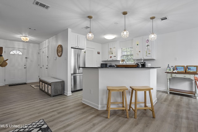 kitchen featuring white cabinetry, light wood-type flooring, stainless steel fridge, a kitchen breakfast bar, and pendant lighting