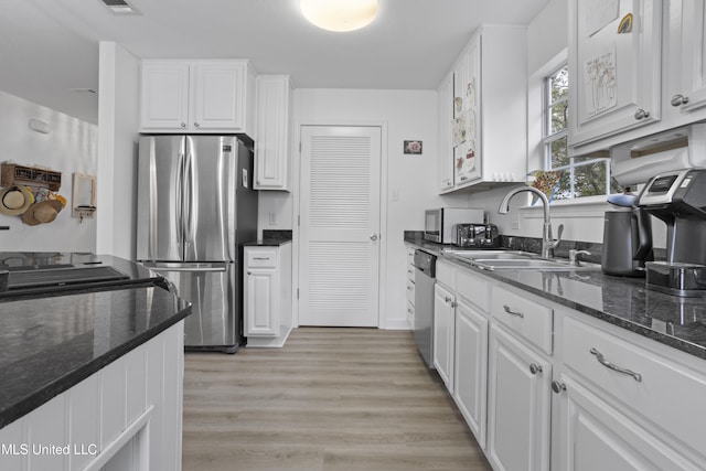 kitchen featuring sink, white cabinetry, light wood-type flooring, dark stone countertops, and stainless steel appliances