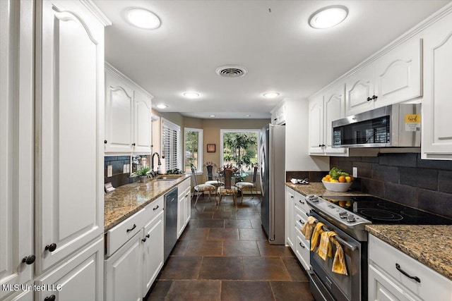 kitchen with white cabinetry, stainless steel appliances, sink, and dark stone counters